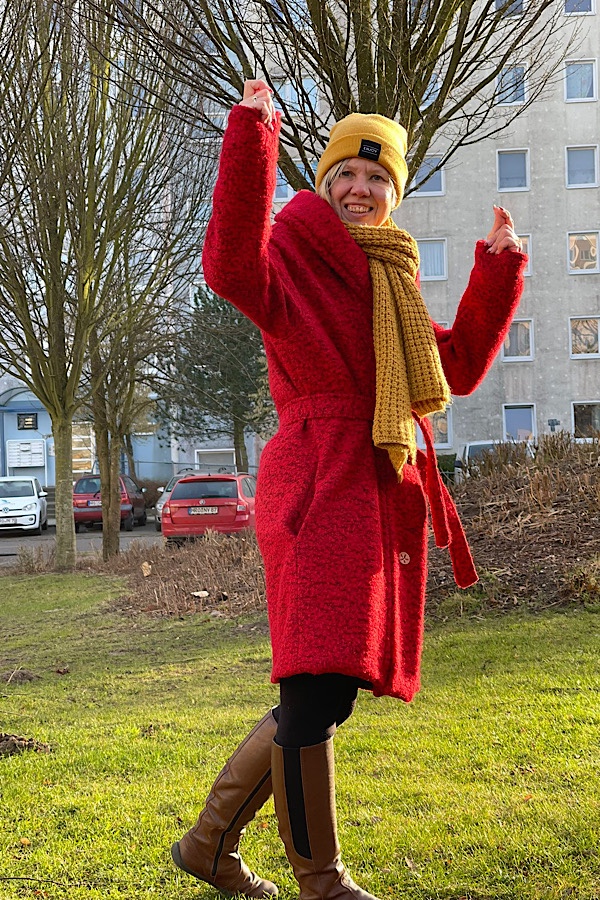 Frau mit erhobenen Armen im roten Mantel