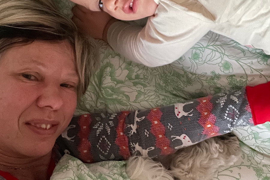 verschlafene Frau mit Hund im Arm und Enkelin daneben früh am Morgen verschlafen im Bett