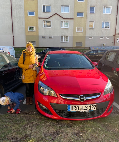 Junge Frau steht links neben einem roten Opel Astra
