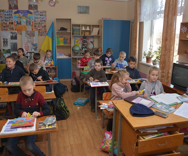 Grundschulkinder sitzen in der Schule an den Schülertischen und lernen freudvoll
