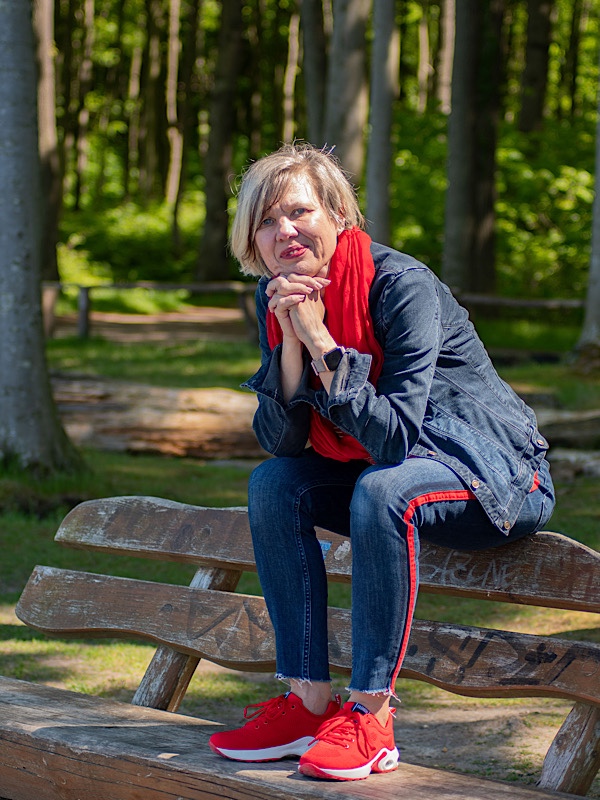 Frau in Jeanskleidung sitzt auf der Lehne einer Holzbank im Wald 