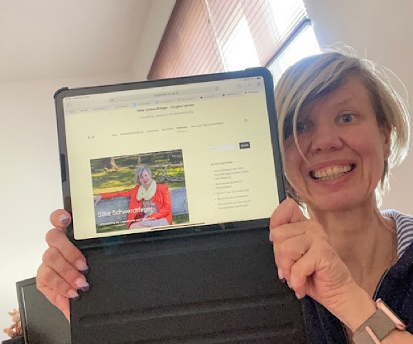 blonde Frau zeigt ihr I-Pad mit ihrer selbstgestalteten Startseite der Website