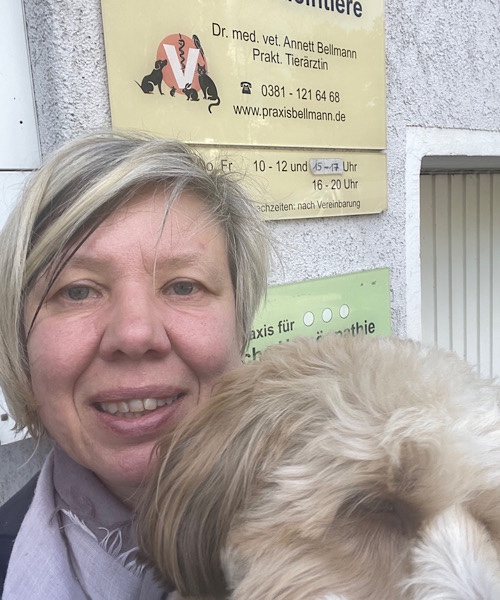 Frau mit Bolonka Zwetna auf dem Arm vor  der Tierarzpraxis