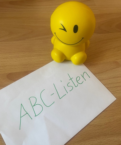 Blatt mit der Aufschrift ABC-Listen und einer freundlichen augenzwinkernden Figur daneben stehend