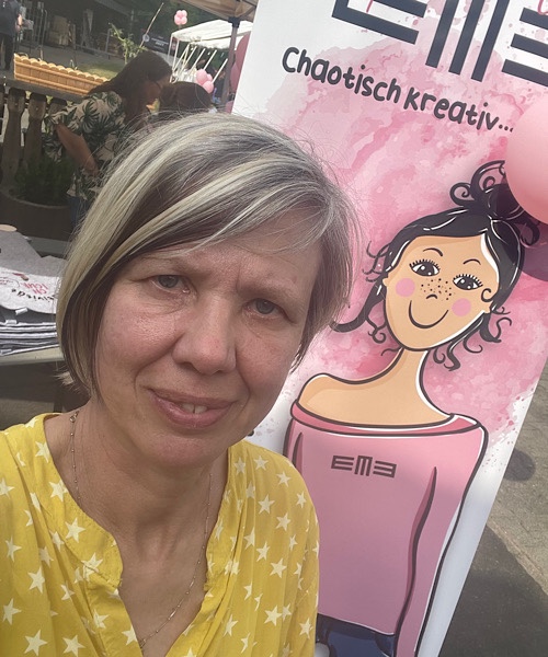 Porträt einer blonden Frau vor dem Plakat mit Eva und der Aufschrift Chaotisch kreativ