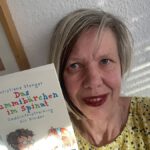 blonde Frau zeigt ein Buch hoch in der Hand zum Thema Gedächtnistraining für Kinder