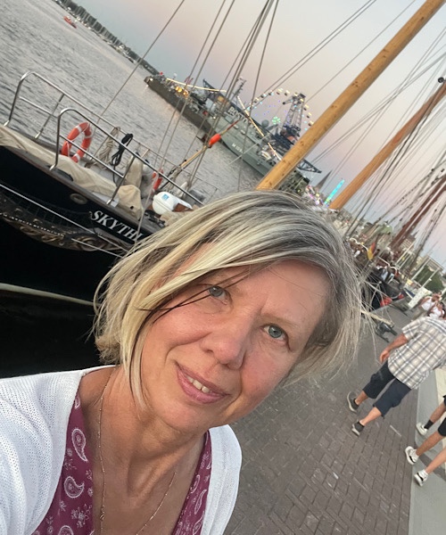 Porträt einer blonden Frau im Vordergrund, Hintergrund Segelschiffe der Hanse Sail in Rostock