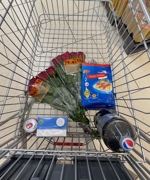 Einkaufswagen mit zwei Sträußen roter Rosen, eine Cola, einmal Milch, Käse und Garnelenspieße