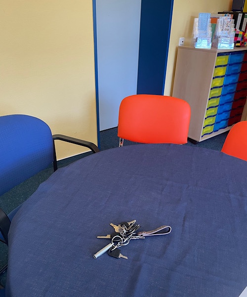 runder Tisch mit blauer Decke, drei Stühle herum, auf dem Tisch liegt ein Schlüsselbund