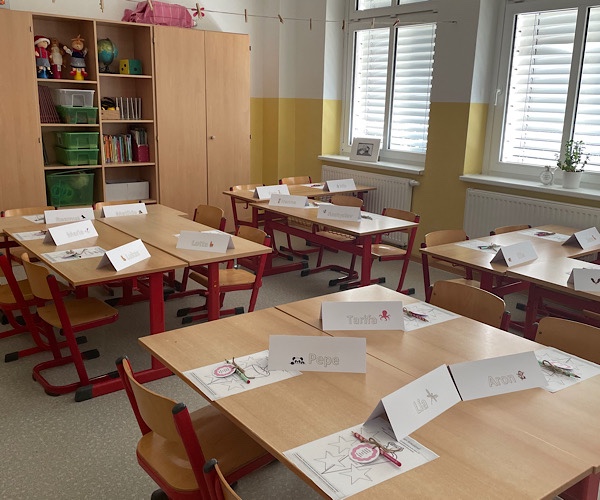 Klassenraum einer Grundschulklasse mit Schulbänken und Stühlen, auf den Tischen liegen Briefe und ein Schreiblernstift mit einem Glückwunsch für die Schulanfänger