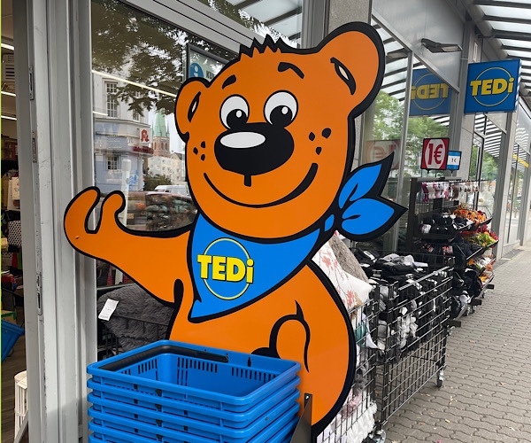 großer Bär von Tedi steht vor dem Geschäft Tedi und hält den Daumen hoch
