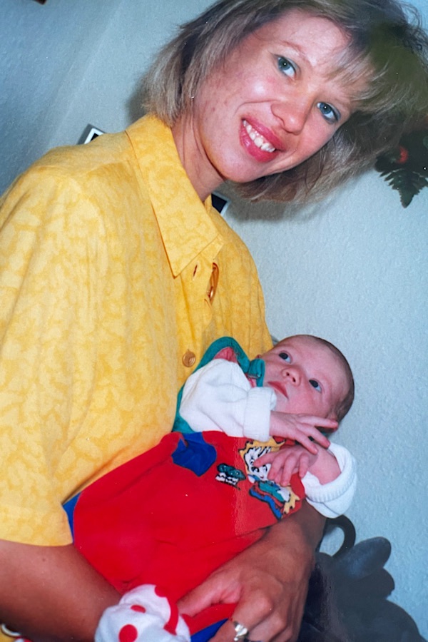 blonde Frau mit Baby im roten Strampler auf dem Arm 