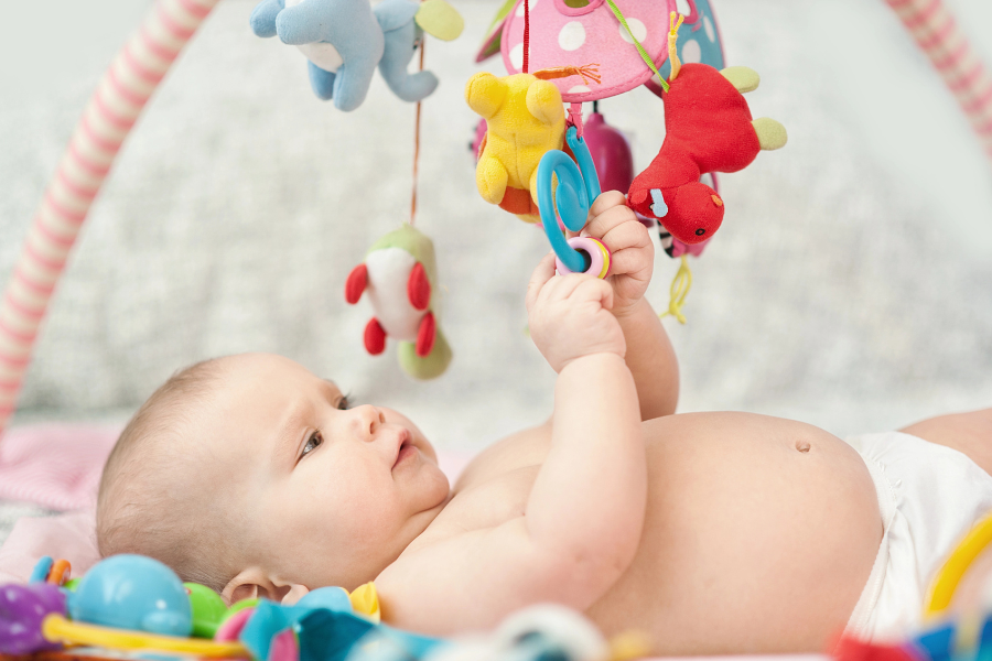 Frühkindliche Reflexe und Lernen: Baby in Rückenlage greift nach Spielzeug