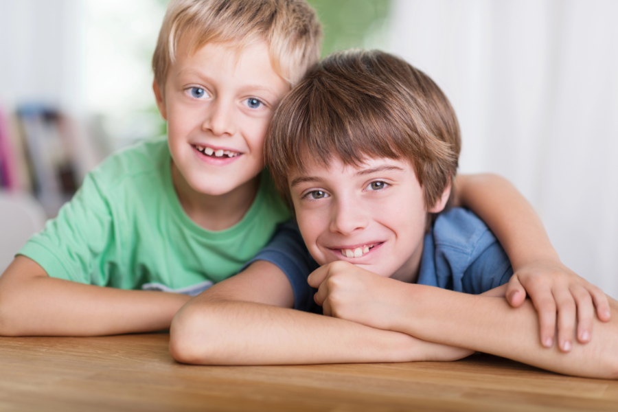 KinFlex® zur emotionalen Stabilität, zwei lachende und sich umarmende Kinder im Sitzen am Tisch