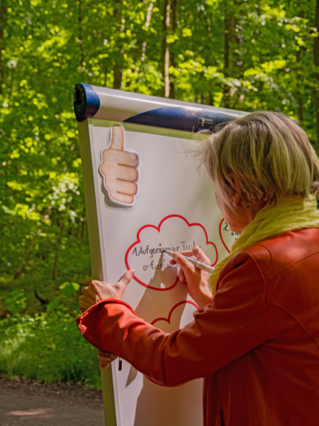 Verbesserung des Gedächtnisses: Konzentriert schreibt blonde Frau in orangefarbener Lederjacke am Flipchart