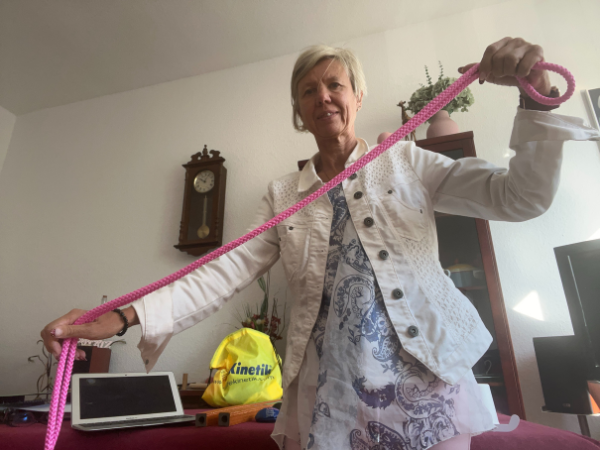 Was ist Life Kinetik? blonde Frau zeigt Life Kinetik Übung mit einem Seil, im Hintergrund befindet sich ein gelber Materialbeutel mit der Aufschrift Life Kinetik