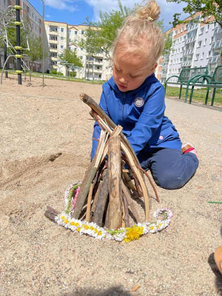 blondes Mädchen baut auf dem Spielplatz mit Stöckchen ein Lagerfeuer