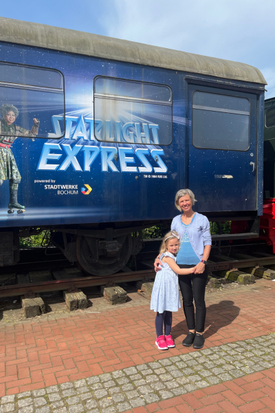 blonde Frau und blaues Mädchen stehen vor dem Wagon mit der Aufschrift "Starlight Express"