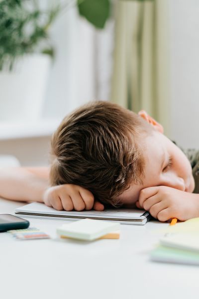 Hochbegabung erkennen: Junge liegt unmotiviert bei den Schulaufgaben mit dem Kopf auf dem Schreibtisch