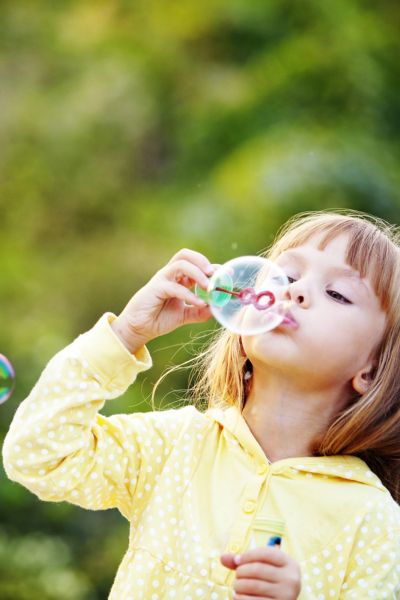 Selbstregulation bei Kindern stärken: Kind im gelben Pulli pustet Seifenblasen