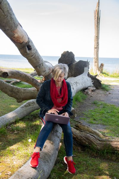 Blogdekade Learnings: Frau in Jeansjacke mit blonden Haaren sitzt auf einem Baumstamm und schreibt am Laptop