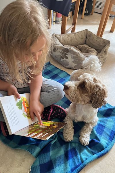 100 Dinge im Familienalltag: Kind und Hund sitzen auf der Decke; Kind liest dem Hund vor