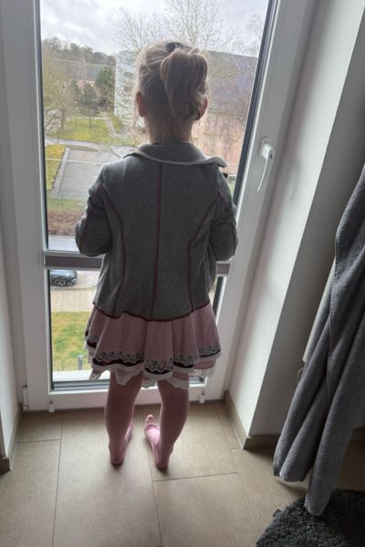 Kindergefühle begleiten: Mädchen mit blonden Haaren steht am Fenster und schaut hinaus