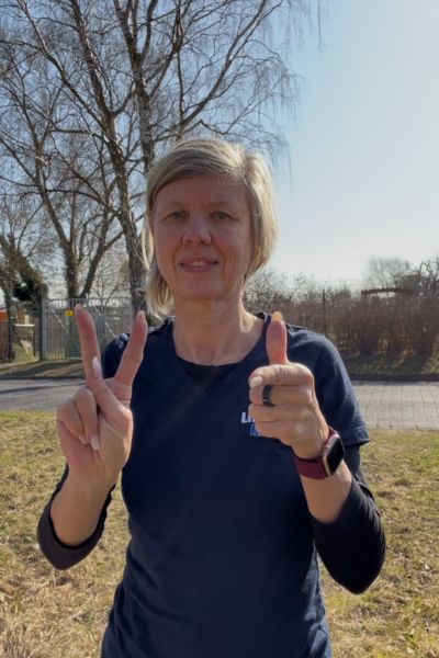 Konzentrationstipps Kinder: blonde Frau im blauen T-Shirt mit der Aufschrift Life Kinetik zeigt die Life Kinetik Übung Hase und Jäger