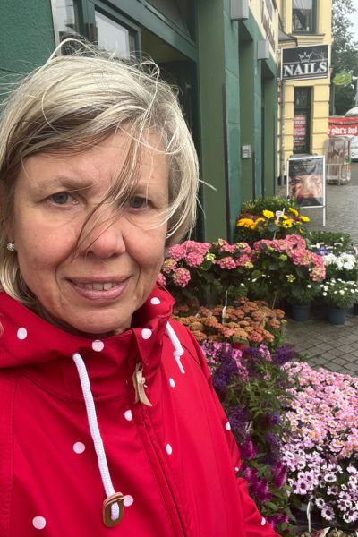 12 von 12 im Juli 2025, blonde Frau in rot gepunkteter Regenjacke steht vor einem Blumengeschäft