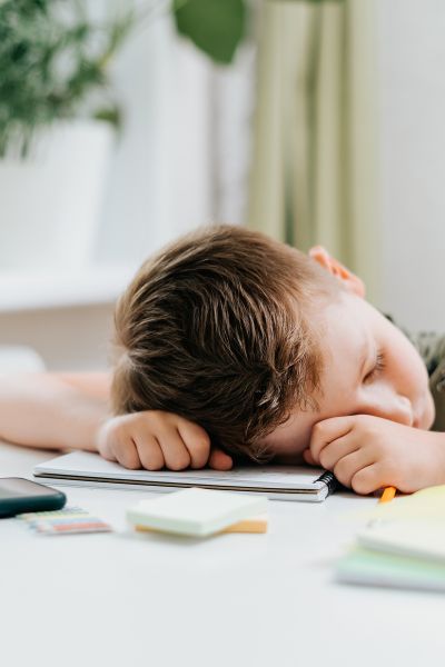 Frühkindliche Reflexe ignorieren; Junge sitzt am Tisch bei den Hausaufgaben; Kopf liegt auf dem Tisch