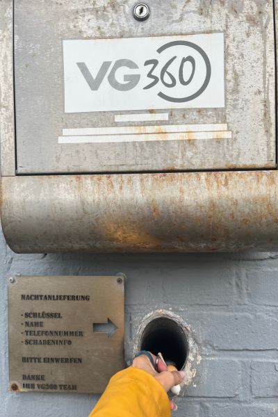 12 von 12 im Oktober 2025; Briefkasten mit der Aufschrift VG 360 an einer grauen Mauerwand, Loch in der Wand, in das eine Hand einen Schlüssel steckt