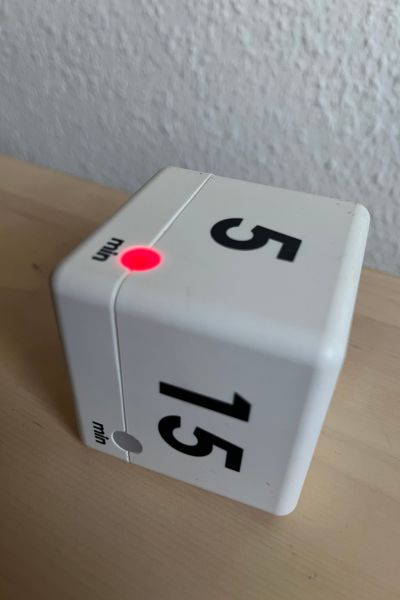 Organisationstipps für Schule und Lernen: Weißer Kurzzeitwecker in der Form eines Würfels mit schwarzen Zahlen; die 5 ist oben, auf der oberen Seite des Würfels leuchtet eine rote Lampe