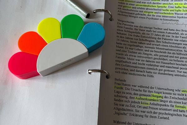 Monatsrückblick 2025: aufgeschlagener Ordner mit beschriebenen Blätter, auf denen Sätze gelb markiert sind; auf der linken Seite liegt eine Textmarker-Sonne mit mehreren Farben