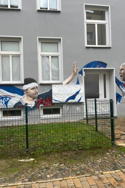 12 von 12 im Oktober 2025; Haus mit Grafity gestaltet; Hansaspieler, Vereinsfahne in blau weiß an Häuserwand gestaltet