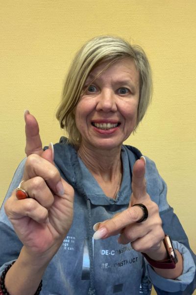 Coaching Alltag anders machen: blonde Frau im blauen Pullover vor gelben Hintergrund zeigt freudig mit beiden Fingern nach vorne