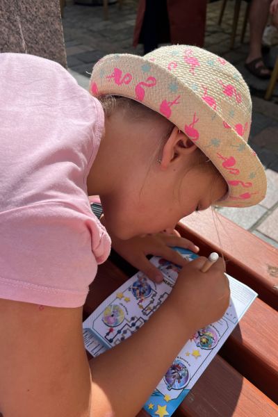 Was ich mit Sorglos lernen bewirken will: Mädchen im rosa Shirt mit Strohhut beugt sich über ein Blatt und schreibt