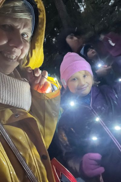 Monatsrückblick Oktober 2025 Sorglos Lernen; Oma in der gelben Regenjacke und Enkelkind in blauer Jacke und rosa Mütze mit Lichterkette im Dunkeln im Rostocker Zoo