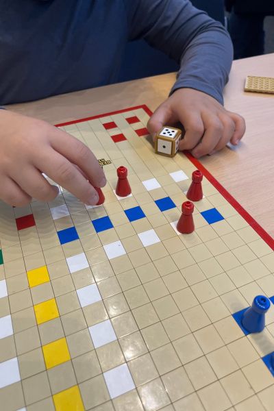 Prognose 2026 Lern und Familiencoaching; Mensch-Ärgere dich nicht-Spiel mit Spielfiguren, eine kindliche Hand führt die rote Spielfigur