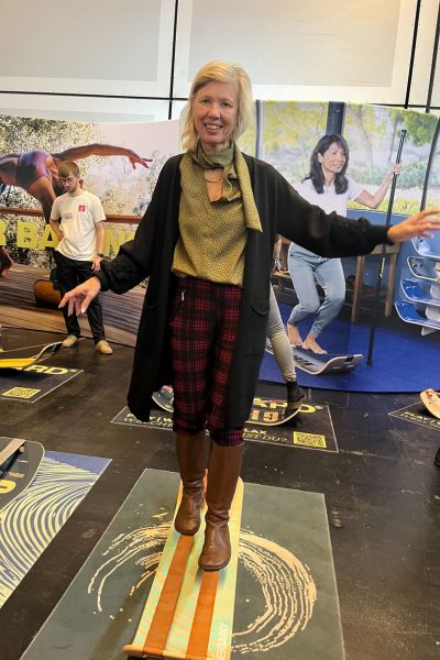 blonde Frau in grüner Bluse und schwarzer Strickjacke balanciert auf einer Slackline