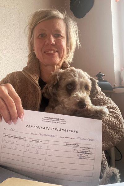 Frau mit Bolonka Zwetna hält eine Zertifikatsverlängerung zum Therapiehund in der Hand.