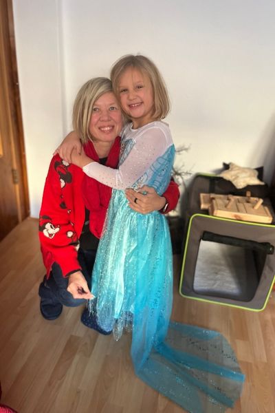 blonde Frau und siebenjähriges Mädchen im Elsakostüm umarmen sich