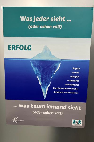 Motto 2026 Tiefe statt Geschwindigkeit: Plakat mit der Aufschrift: Was jeder sieht (oder sehen will) Eisberg mit der aus dem Wasser herausragendem Teil und dem viel größeren Teil unter Wasser, was kaum jemand sehen will