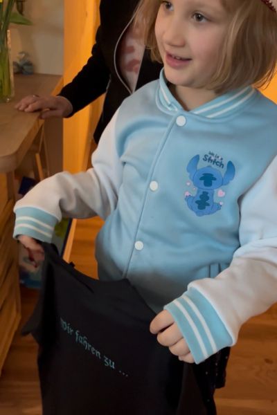 Monatsrückblick Januar 2026: achtjähriges Mädchen mit dunklem T-Shirt in der Hand mit der Aufschrift "Wir fahren zu ..." schaut staunend.