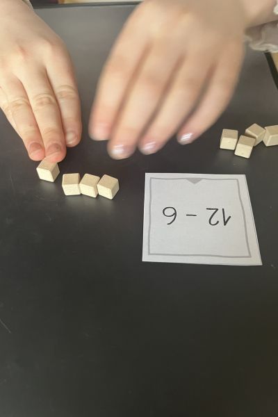 Rechenprobleme Grundschule: Hände eines Kindes legen kleine Würfel zur Aufgabe 12-6