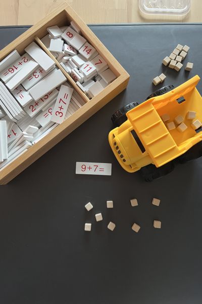 Rechenprobleme Grundschule: Holzkiste mit Grundaufgaben, kleiner gelber Bagger transportiert kleine Würfel, Aufgabe wird gelegt
