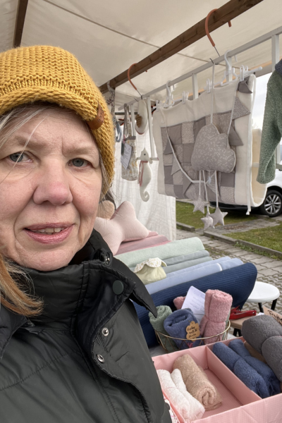 12 von 12 im April 2026: Frau mit senffarbener Strickmütze  vor einem Stoffstand auf dem Stoffmarkt