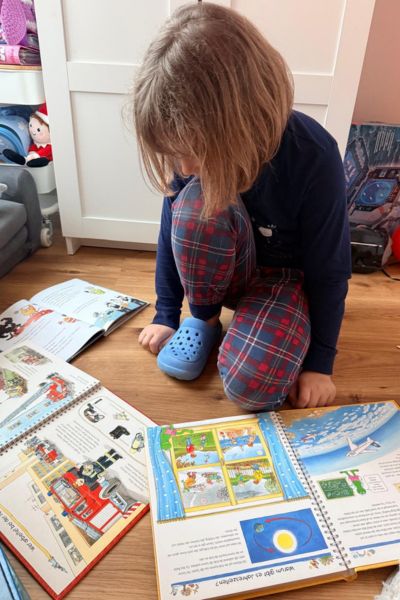 Lerncoaching Kinder Lernprobleme: blondes Mädchen sitzt vor mehreren Büchern und kann sich nicht entscheiden