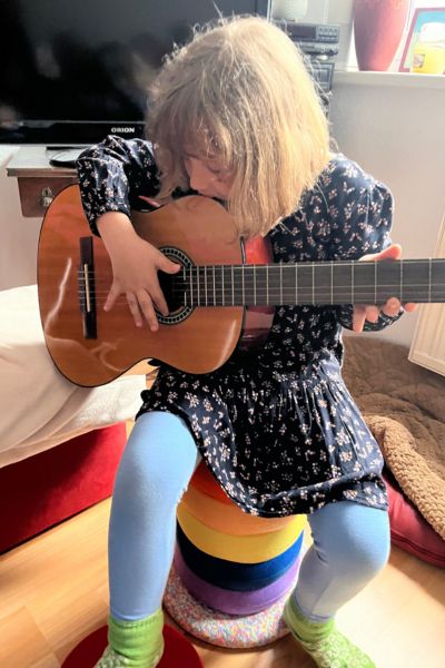 Lerncoaching Kinder Lernprobleme: blondes Mädchen sitzt auf Stapelsteinen und spielt Gitarre