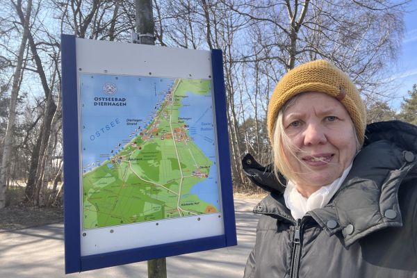 ADHS Kind Lernen: blonde Frau mit senffarbener Strickmütze steht vor einer Karte auf dem der Ort Dierhagen eingezeichnet ist