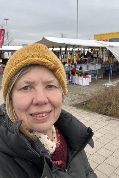Lernen und Familie: Frau mit senffarbener Mütze vor Ständen der Stoffhändler